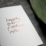 A rose gold hand foiled wedding card saying Happily Ever Fucking After 