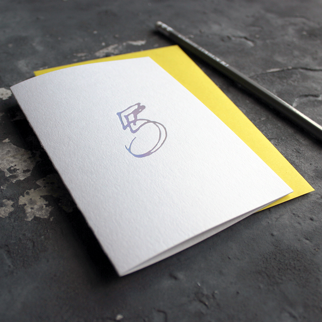 A fifth birthday card with a hand drawn number five hand pressed in holographic foil on the front and a yellow envelope