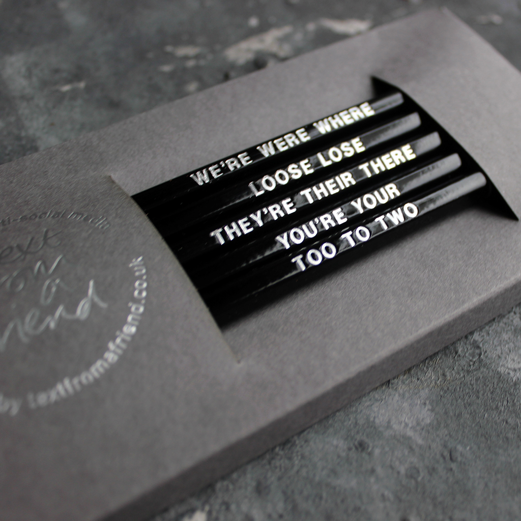 Black HB pencils printed with silver foil phrases and packaged in a grey paper box. 