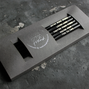 Black HB pencils printed with silver foil phrases and packaged in a grey paper box. 