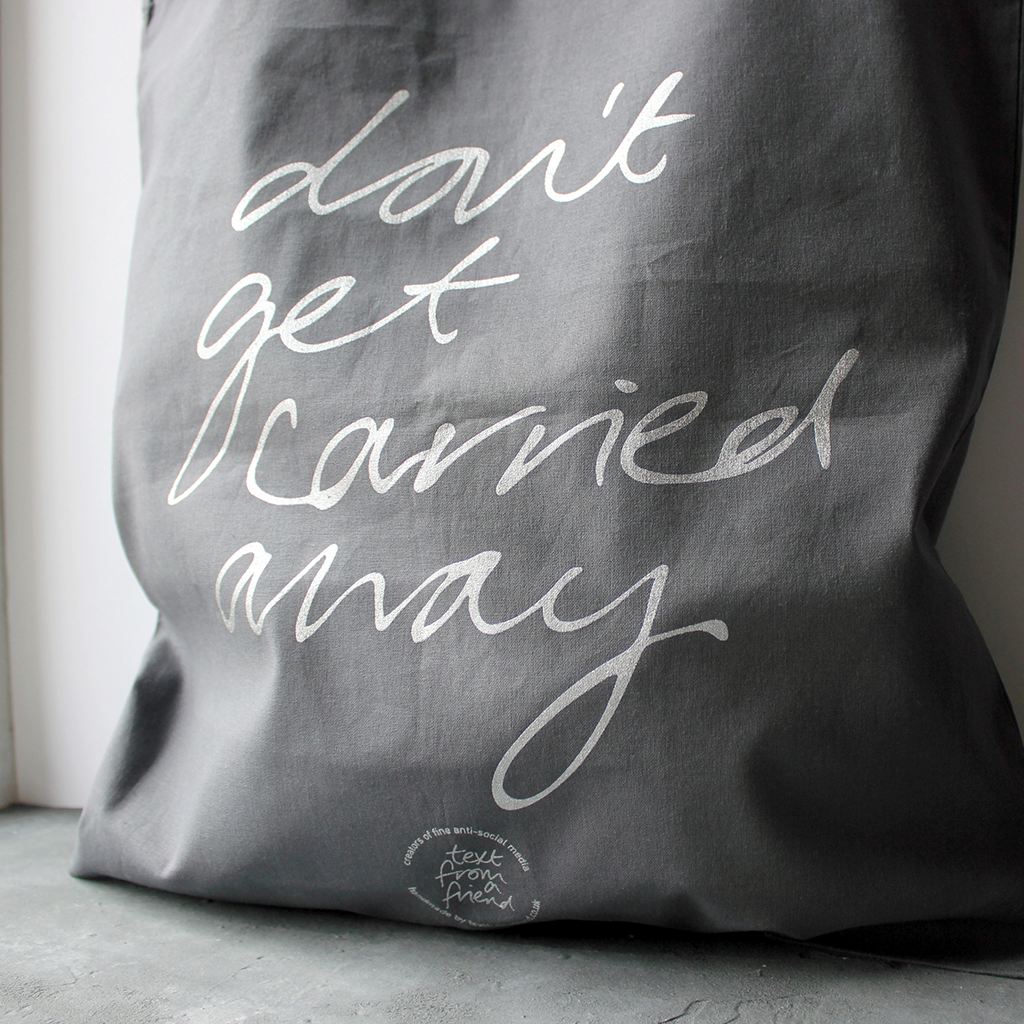 100% cotton grey tote bag hand screen printed in silver metallic ink with a handwritten message that says 'don't get carried away' 