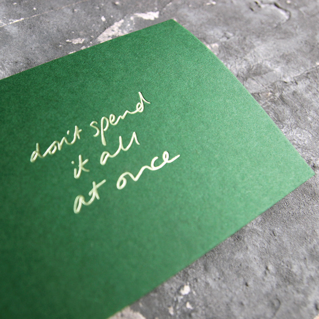 This cash card says Don't Spend It All At Once and is handwritten and hand printed in pale green foil on green luxury paper on grey board
