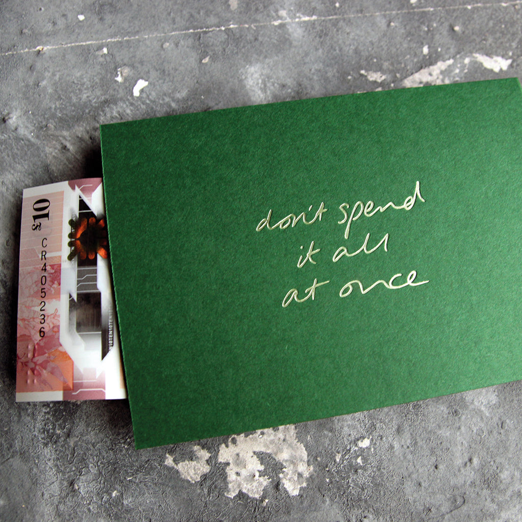 This cash card says Don't Spend It All At Once and is handwritten and hand printed in pale green foil on green luxury paper on grey board