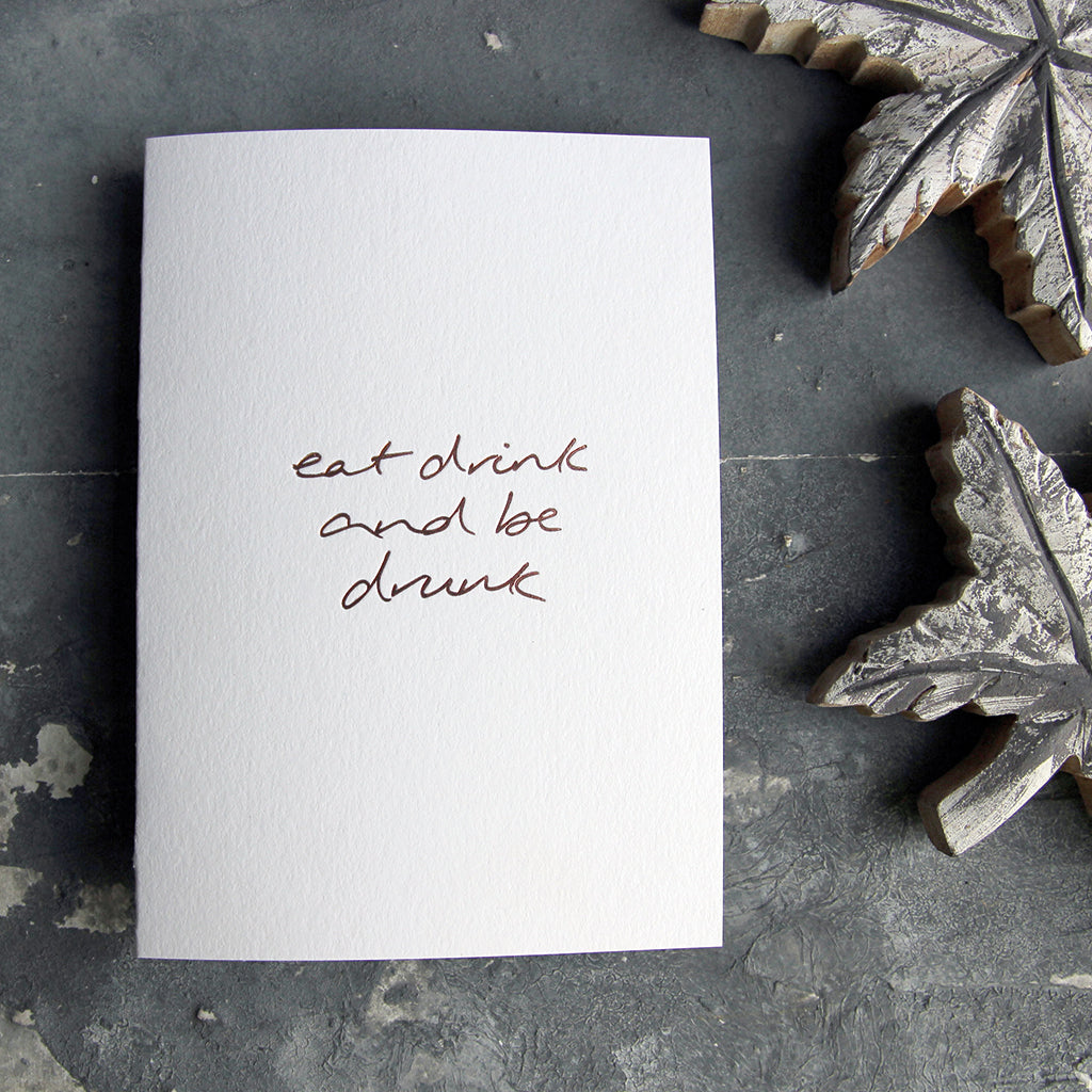 This christmas card says Eat Drink And Be Drunk on hand foiled on white luxury paper on grey board