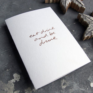 This christmas card says Eat Drink And Be Drunk on hand foiled on white luxury paper on grey board
