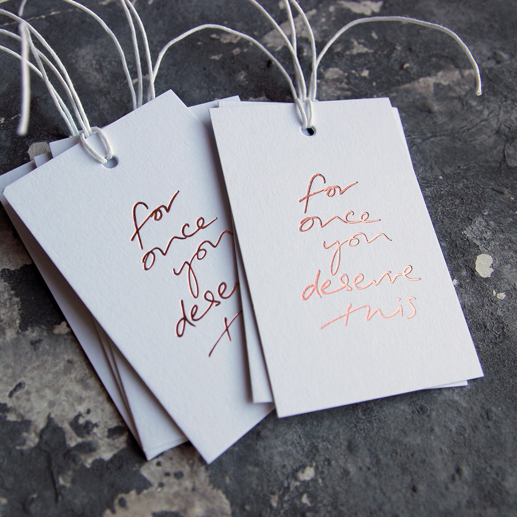 This cash card saPack of gift tags say For Once You Deserve This handwritten and hand printed in rose gold foil on white luxury paper on grey board