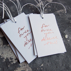 This cash card saPack of gift tags say For Once You Deserve This handwritten and hand printed in rose gold foil on white luxury paper on grey board