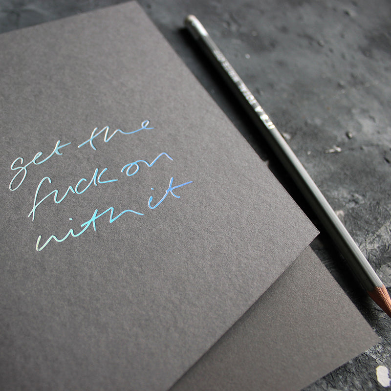 a grey handmade luxury notebook that's hand foiled with the message Get The Fuck On With It in holographic foil