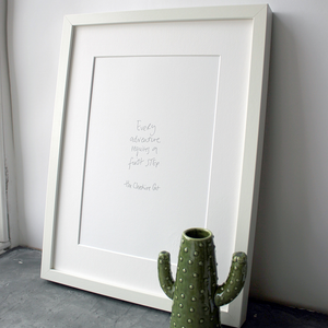This handwritten children's cheshire cat print says 'Every Adventure Requires A First Step' in grey on white paper. 