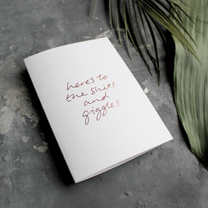 The front of the card has the phrase 'here's to the shits and giggles' handwritten and hand pressed in rose gold foil