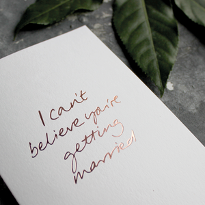 The front of the card has the phrase 'I can't believe you're getting married' handwritten and hand pressed in rose gold foil