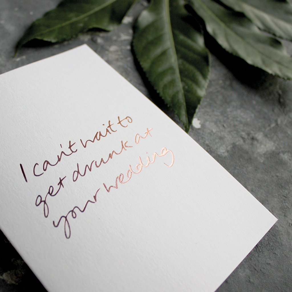 The front of the card has the phrase 'I can't wait to get drunk at your wedding' handwritten and hand pressed in rose gold foil