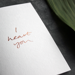 a luxury card that is handwritten with a rose gold foil message saying I Heart You