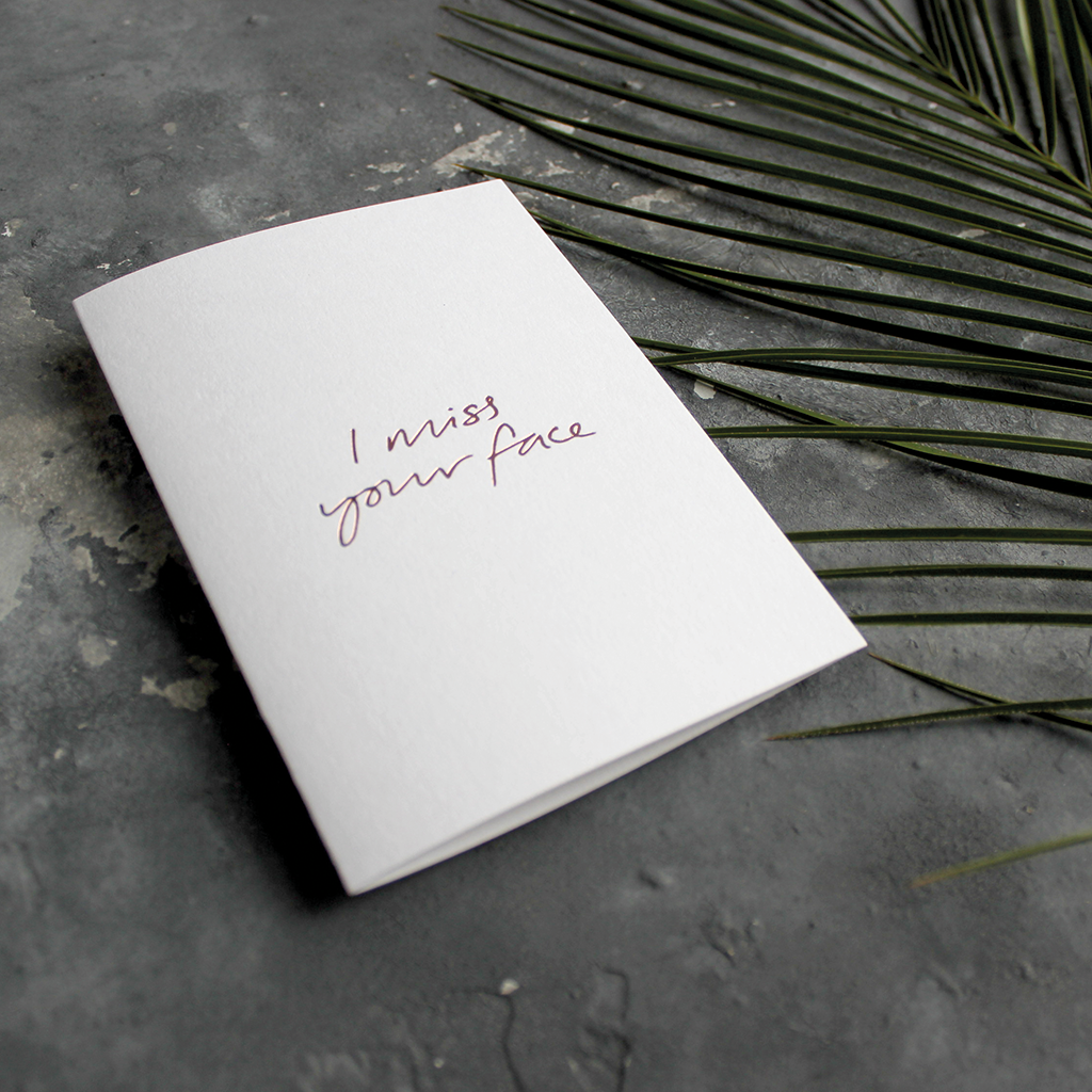 The front of this luxury card says I Miss Your Face, handwritten and hand foiled in rose gold foil