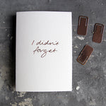 This birthday card says I Didn't Forget is handwritten design and handfoiled in rose gold foil on luxury white paper, photographed on a grey board 