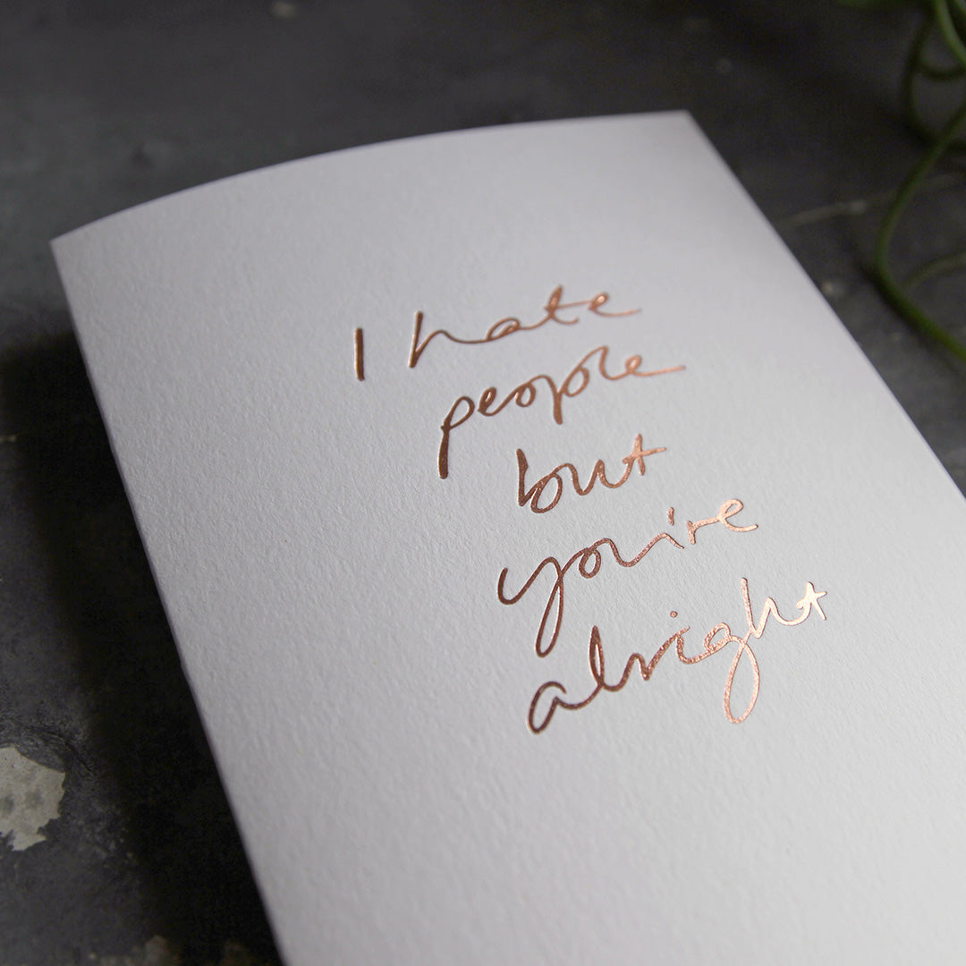this hand foiled luxury white card says I Hate People But You're Alright on the front in rose gold foil