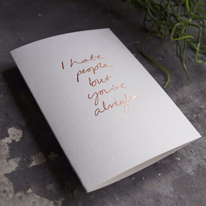 this hand foiled luxury white card says I Hate People But You're Alright on the front in rose gold foil