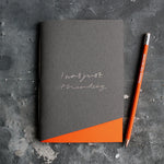 a grey and orange handmade luxury notebook that's hand foiled with the message I Was Just Thinking in holographic foil