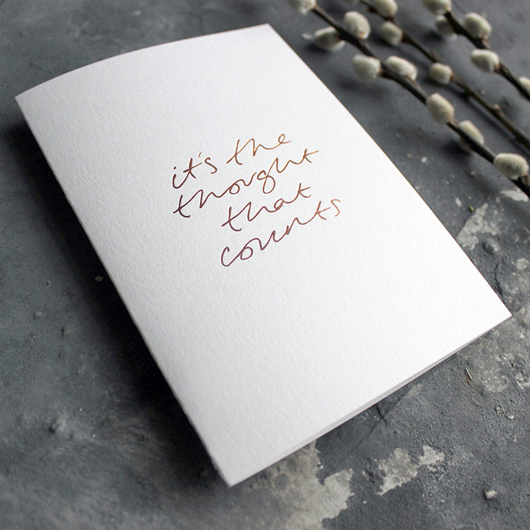 This rose gold hand foiled luxury white card says It's The Thought That Counts on the front in handwriting from Text From A Friend