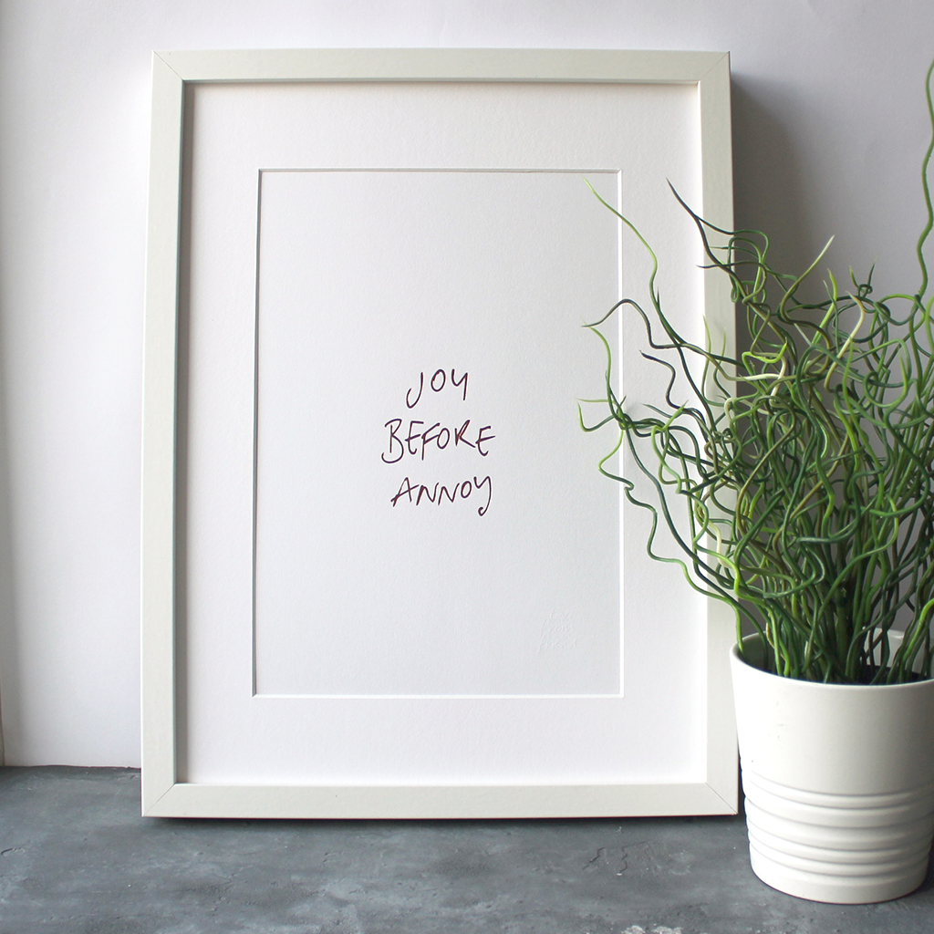 This unframed rose gold foil print has the words Joy before Annoy handwritten in a contemporary design