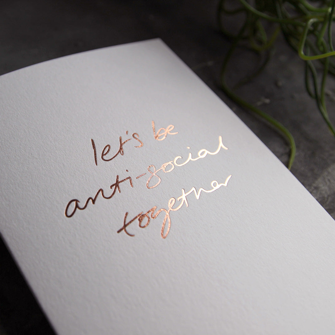this hand foiled luxury white card says Let's Be Anti Social Together on the front in rose gold foil