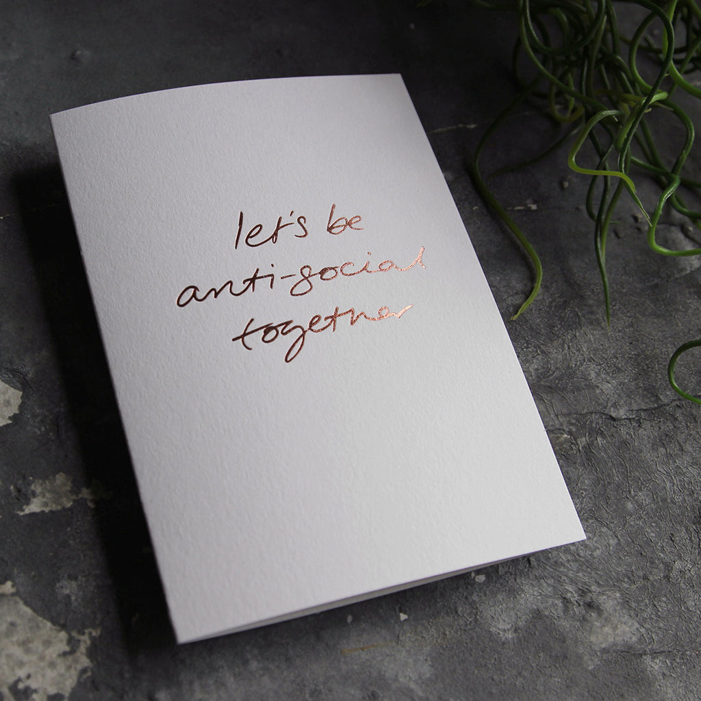 this hand foiled luxury white card says Let's Be Anti Social Together on the front in rose gold foil