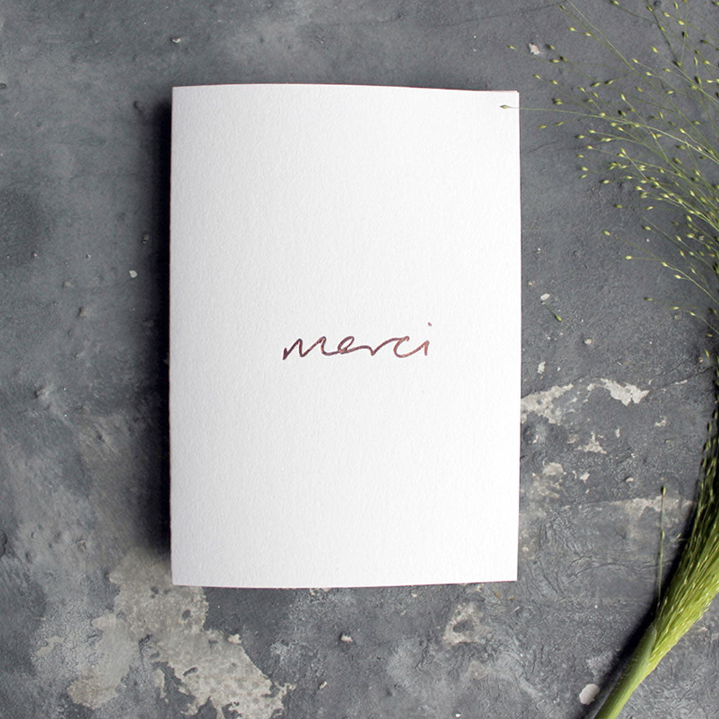 this white luxury card is hand foiled with the phrase Merci on the front