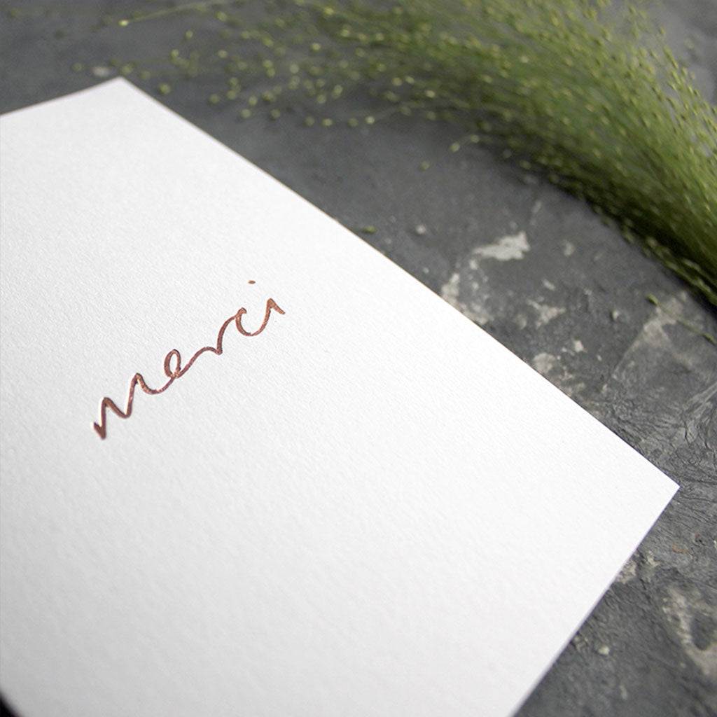 this white luxury card is hand foiled with the phrase Merci on the front