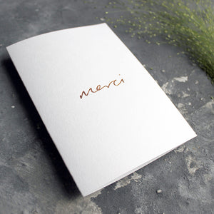 this white luxury card is hand foiled with the phrase Merci on the front