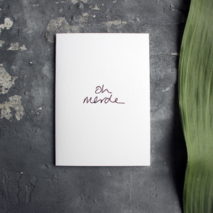 a luxury handwritten rose gold hand foiled message says Oh Merde on the front of the card