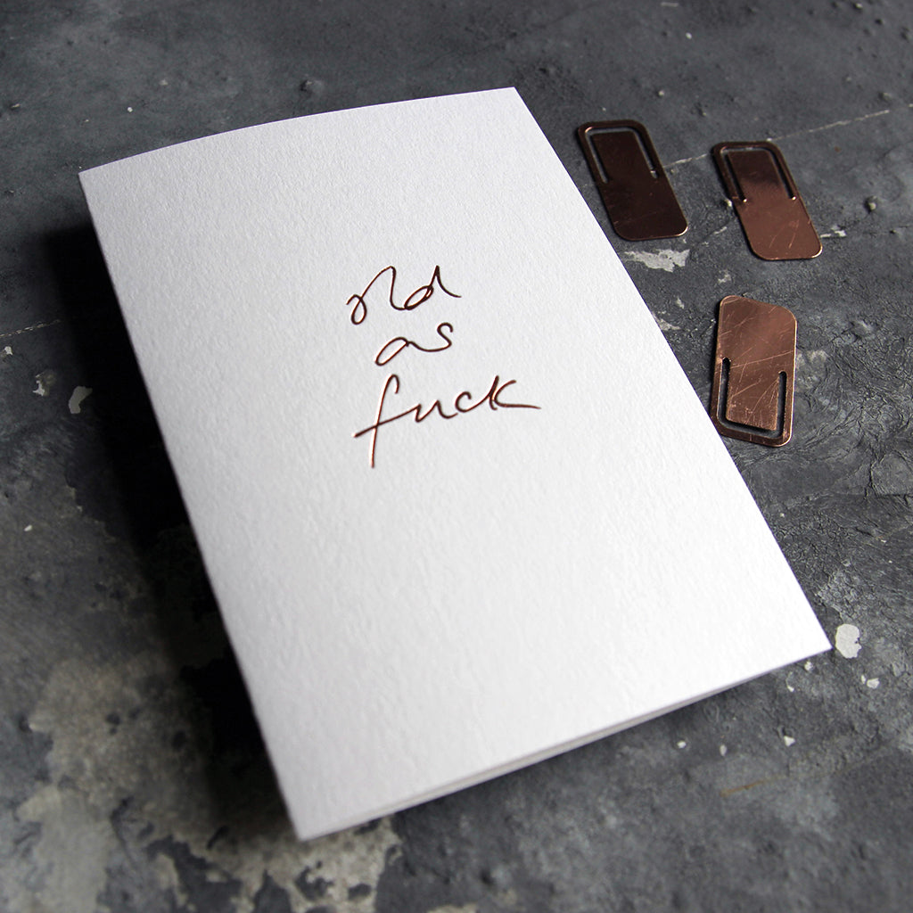 This birthday card says Old As Fuck is handwritten design and handfoiled in rose gold foil on luxury white paper, photographed on a grey board 