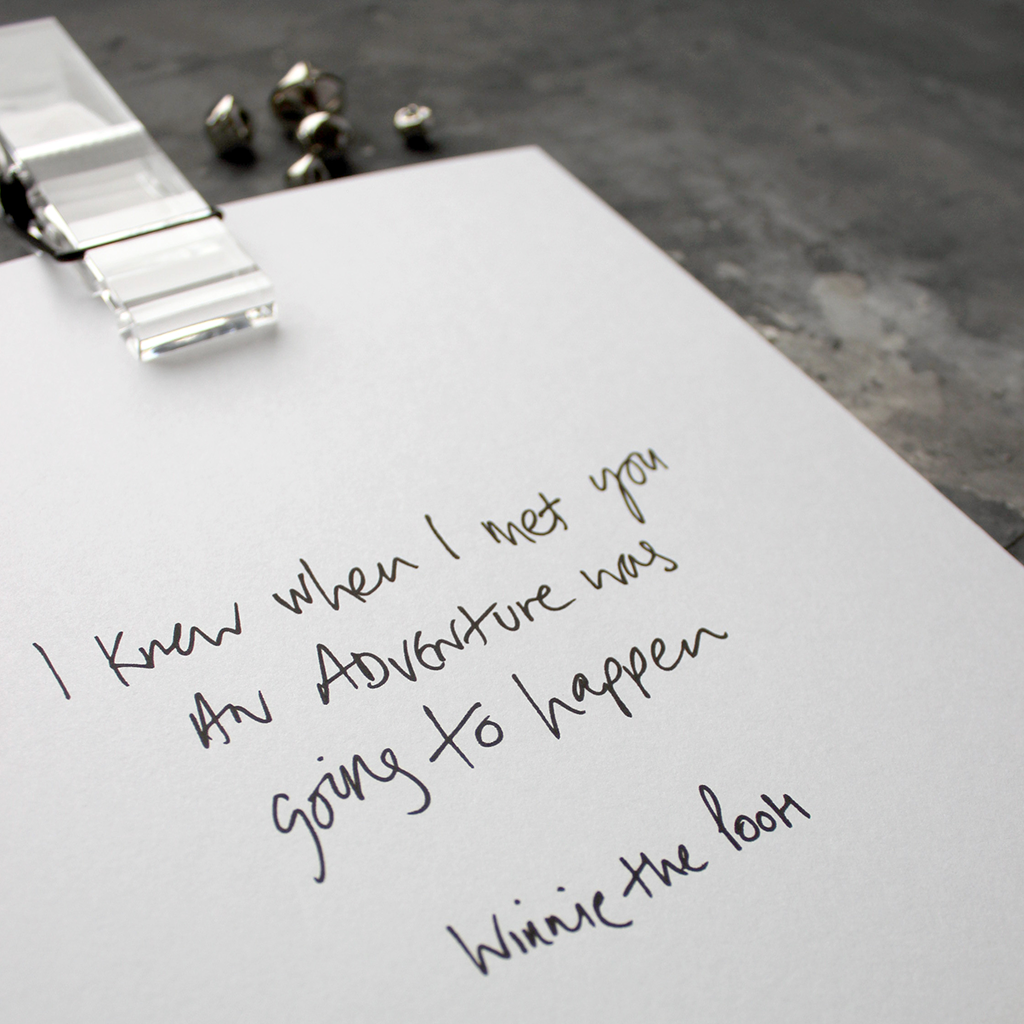 This handwritten children's Winnie The Pooh print says 'I Knew When I Met You An Adventure Was Going To Happen' in black on white paper.