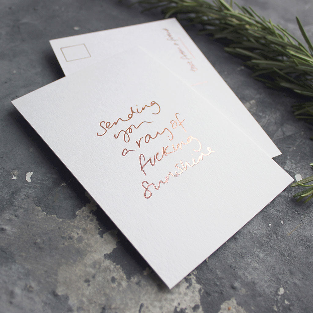 The Sending You A Ray Of Fucking Sunshine postcard is hand printed both sides in rose gold foil 