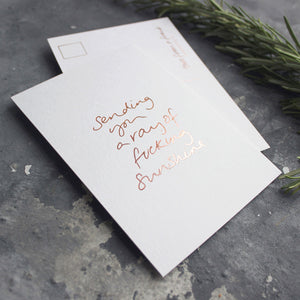 The Sending You A Ray Of Fucking Sunshine postcard is hand printed both sides in rose gold foil 