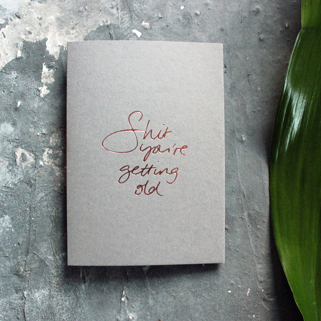 A luxury grey birthday card with the message 'Shit you're getting old' hand written and hand foiled in rose gold