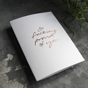 this hand foiled luxury white card says So Fucking Proud Of You on the front in rose gold foil