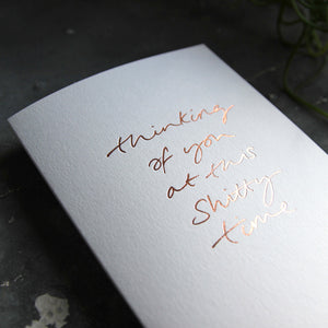 this hand foiled luxury white card says Thinking Of You At This Shitty Time on the front in rose gold foil