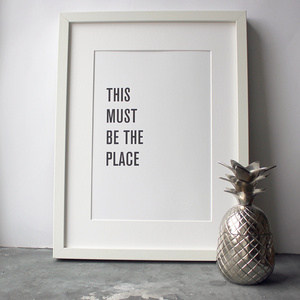 A framed print in a black and white typographic design which says 'This Must Be The Place' by Talking Heads