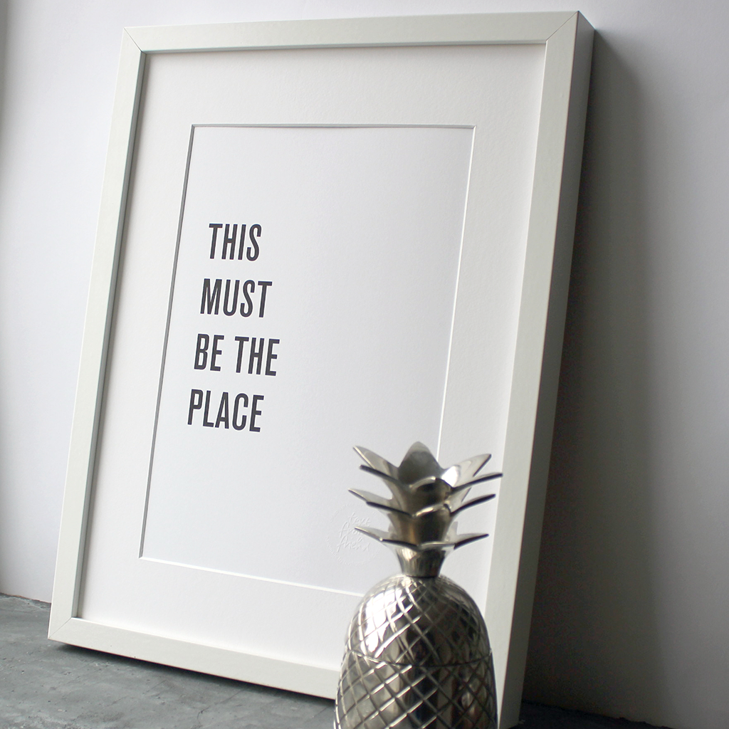 A framed print in a black and white typographic design which says 'This Must Be The Place' by Talking Heads
