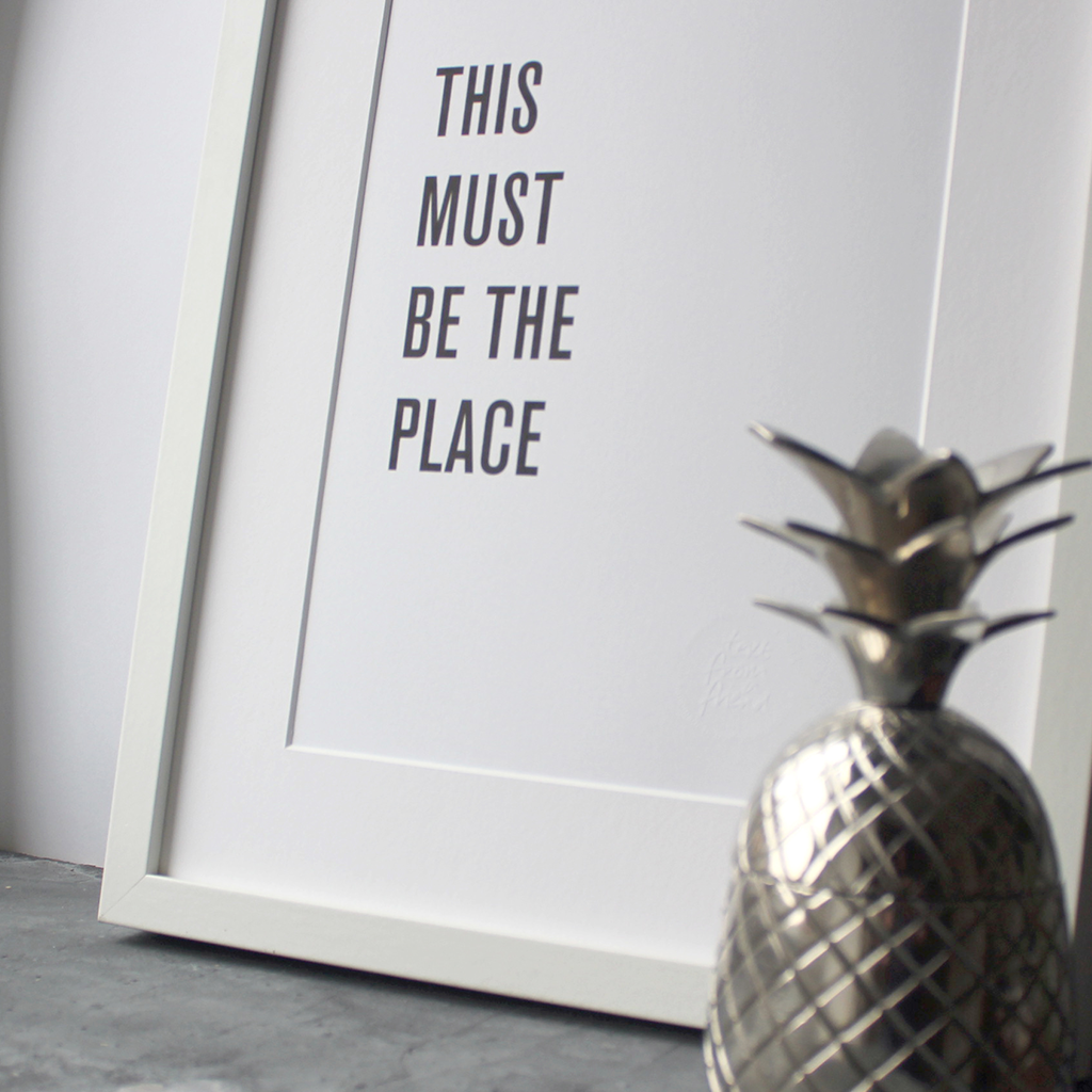 A framed print in a black and white typographic design which says 'This Must Be The Place' by Talking Heads