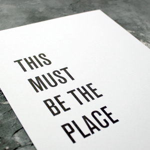 A framed print in a black and white typographic design which says 'This Must Be The Place' by Talking Heads