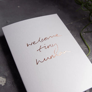 this hand foiled luxury white card says Welcome Tiny Human on the front in rose gold foil