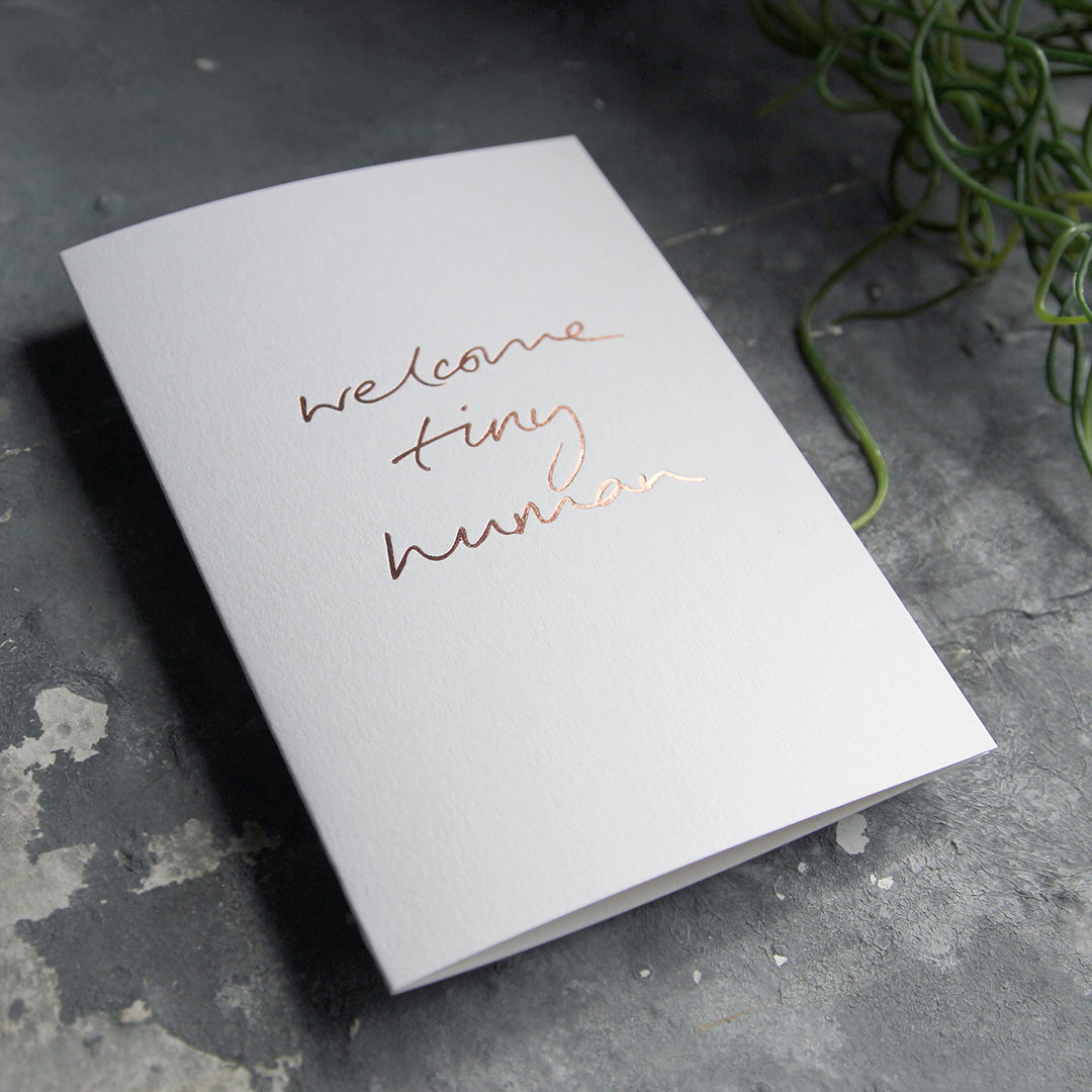 this hand foiled luxury white card says Welcome Tiny Human on the front in rose gold foil