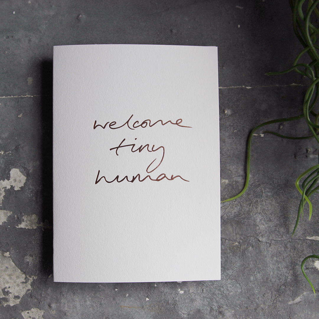 this hand foiled luxury white card says Welcome Tiny Human on the front in rose gold foil