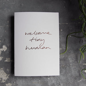 this hand foiled luxury white card says Welcome Tiny Human on the front in rose gold foil