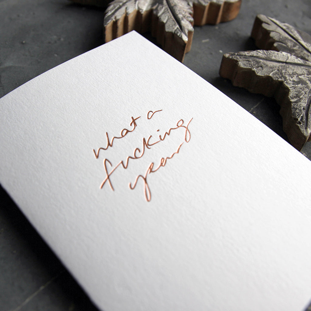 This christmas card says What A Fucking Year on hand foiled on white luxury paper on grey board