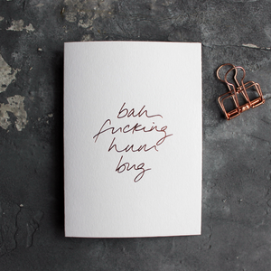 This white christmas card has 'Bah Fucking Hum Bug' handprinted in rose gold foil in handwriting on the front.