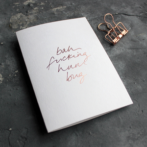 This white christmas card has 'Bah Fucking Hum Bug' handprinted in rose gold foil in handwriting on the front.