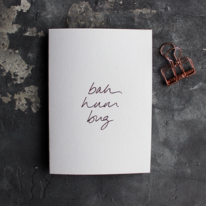 This white christmas card has 'Bah Hum Bug' handprinted in rose gold foil in handwriting on the front.