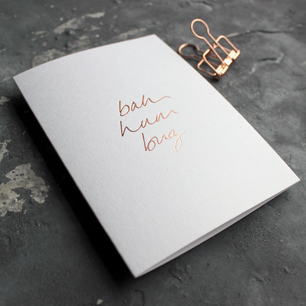 This white christmas card has 'Bah Hum Bug' handprinted in rose gold foil in handwriting on the front.